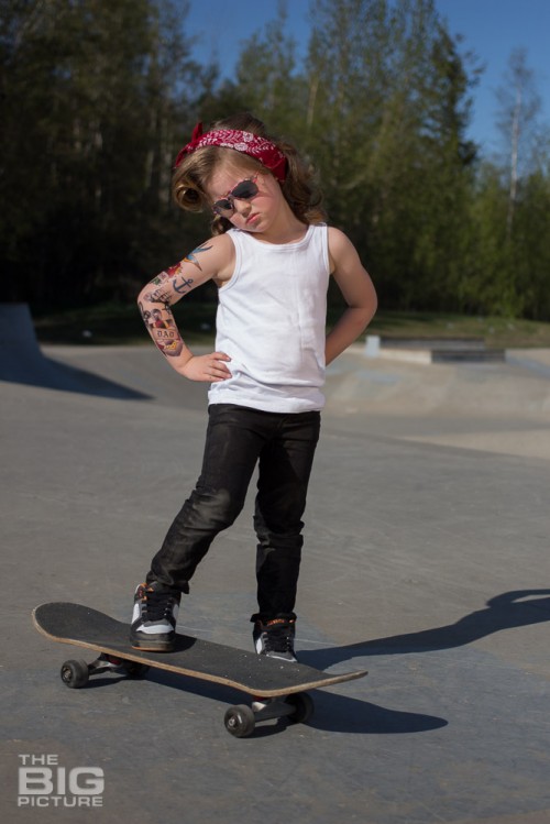 children's portraits, little skater girl with retro hair and fake tattoo sleeve standing on a skateboard in a skate park on a sunny day, children's photography, skater girl